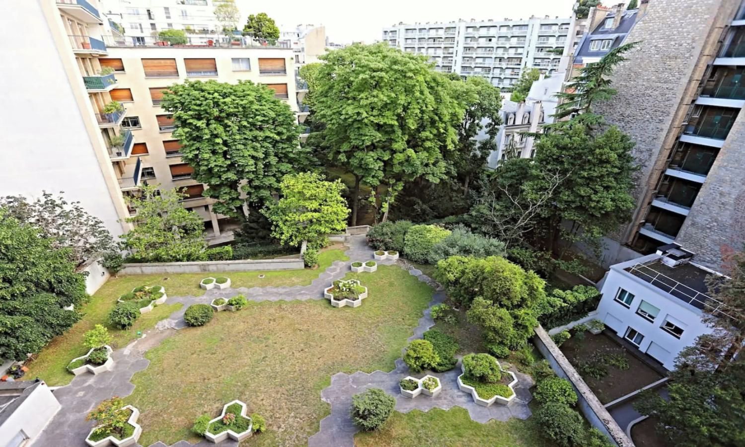 A courtyard with multiple trees, a central lawn, and surrounding buildings.