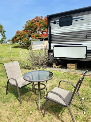 A recreational vehicle with a white panel, a glass table, and two chairs in a grassy area. - Awesome recreational vehicle on a gorgeous plot of land! Very private and safe. (Aguadilla)