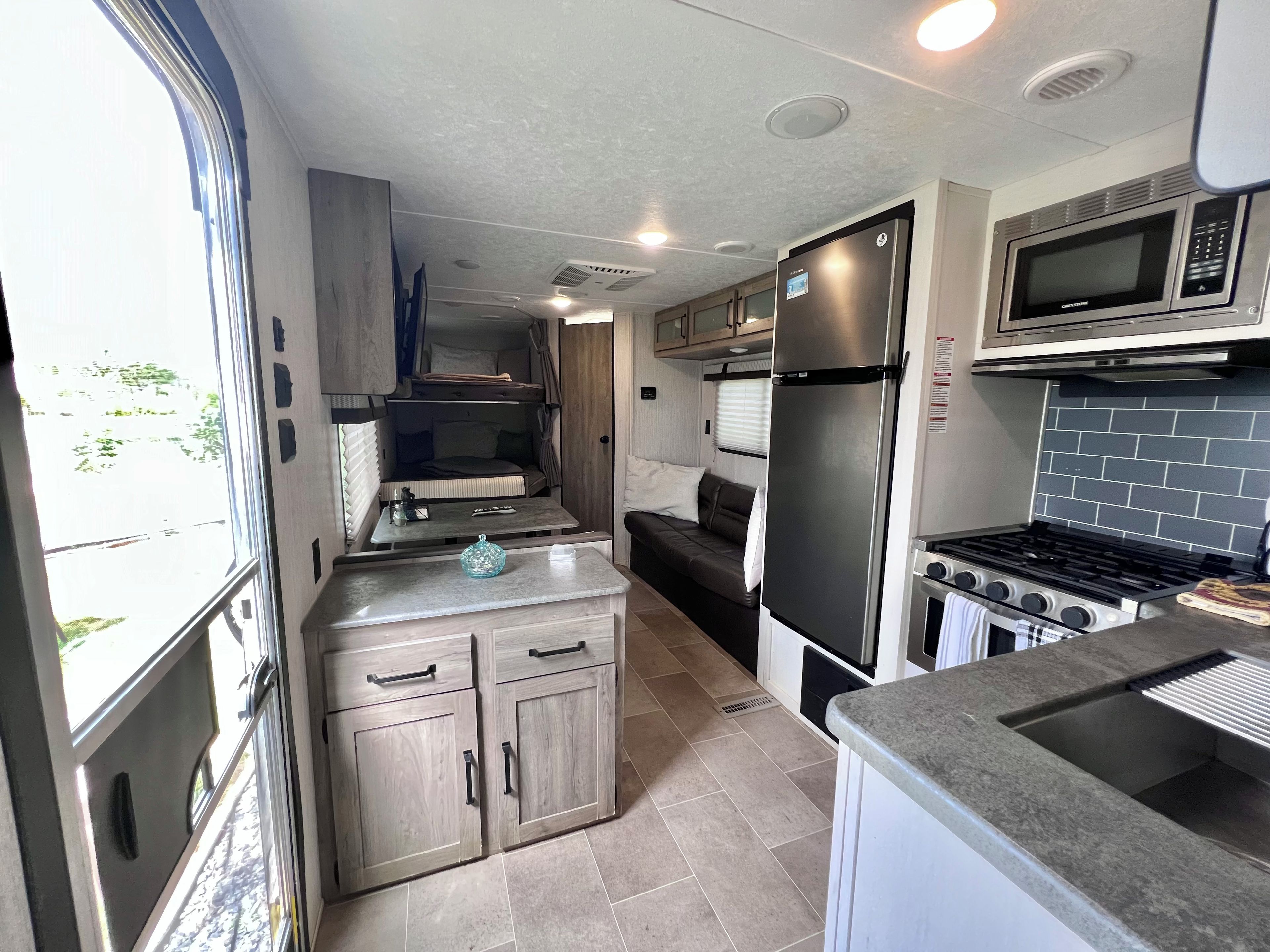 Une cuisine compacte pour camping-car, équipée d’un réfrigérateur, d’un four à micro-ondes, d’une cuisinière et d’un petit coin repas.