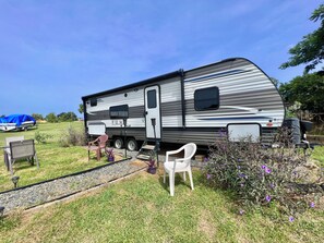 A recreational vehicle parked in a grassy area with a small patio setup including a white chair and a table. - Awesome recreational vehicle on a gorgeous plot of land! Very private and safe. (Aguadilla)