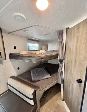 A compact RV interior with a bunk bed, a small seating area, and a window with blinds. - Awesome recreational vehicle on a gorgeous plot of land! Very private and safe. (Aguadilla)
