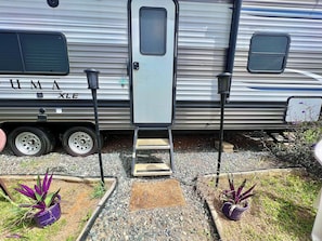 A recreational vehicle with a sliding door, a step leading up to the entrance, and potted plants in the foreground. - Awesome recreational vehicle on a gorgeous plot of land! Very private and safe. (Aguadilla)