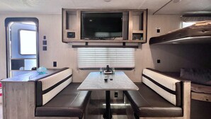 Een compact camperinterieur met een kitchenette, een flatscreen-tv en een eethoek met bankzitplaatsen.
