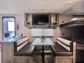 A compact RV interior with a kitchenette, a flat-screen TV, and a dining area with bench seating. - Awesome recreational vehicle on a gorgeous plot of land! Very private and safe. (Aguadilla)