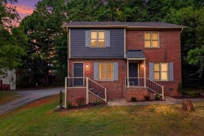 A two-story brick house with a front porch and a small garden. - Cozy Raleigh Stay for 6 Near NC State and RDU (Raleigh)