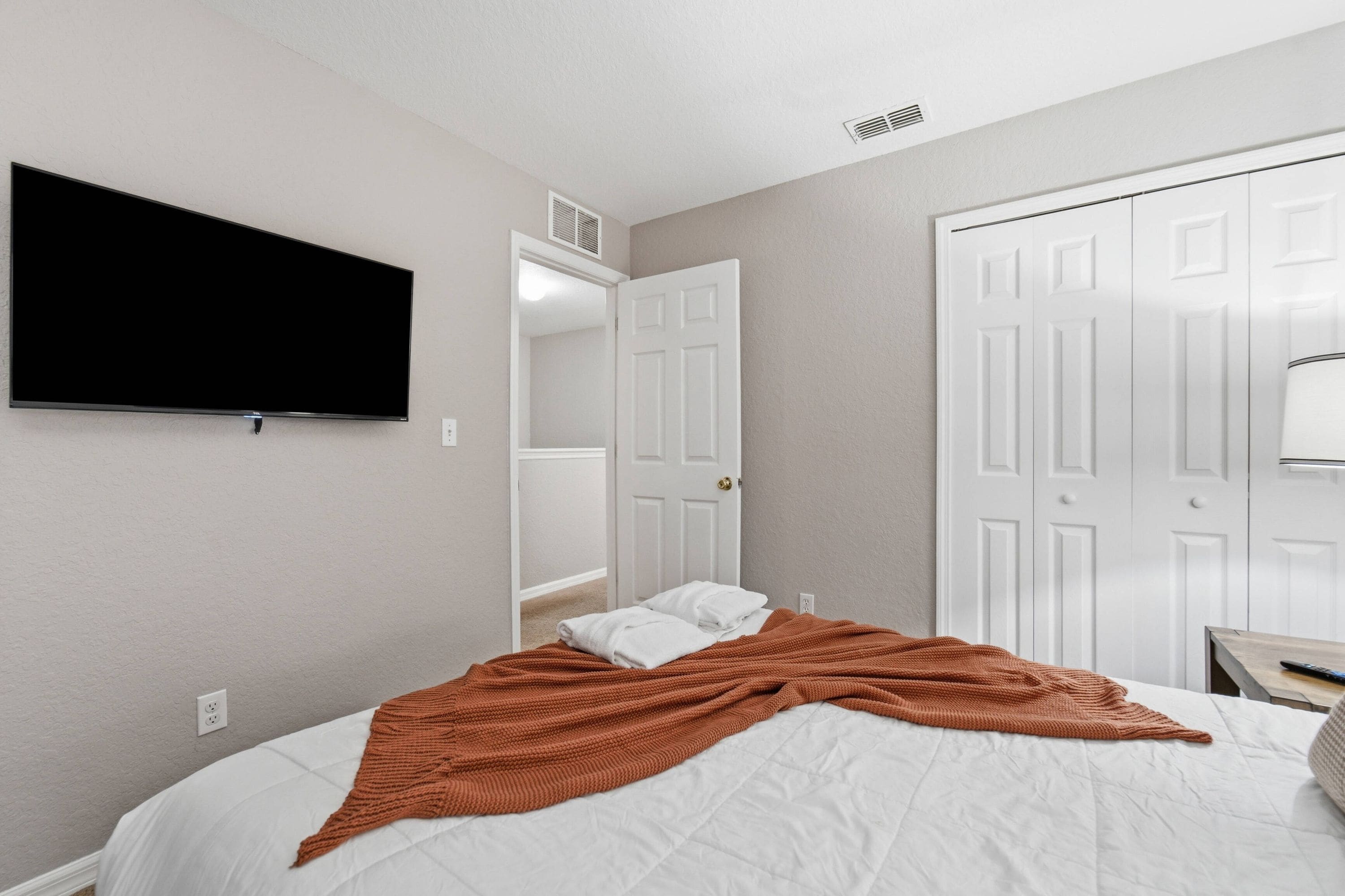 A bedroom with a bed, a television mounted on the wall, and a door.