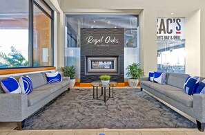 A modern lounge area with grey sofas, a patterned rug, and a wall-mounted fireplace. - 4BR Townhouse at Regal Oaks (Kissimmee)