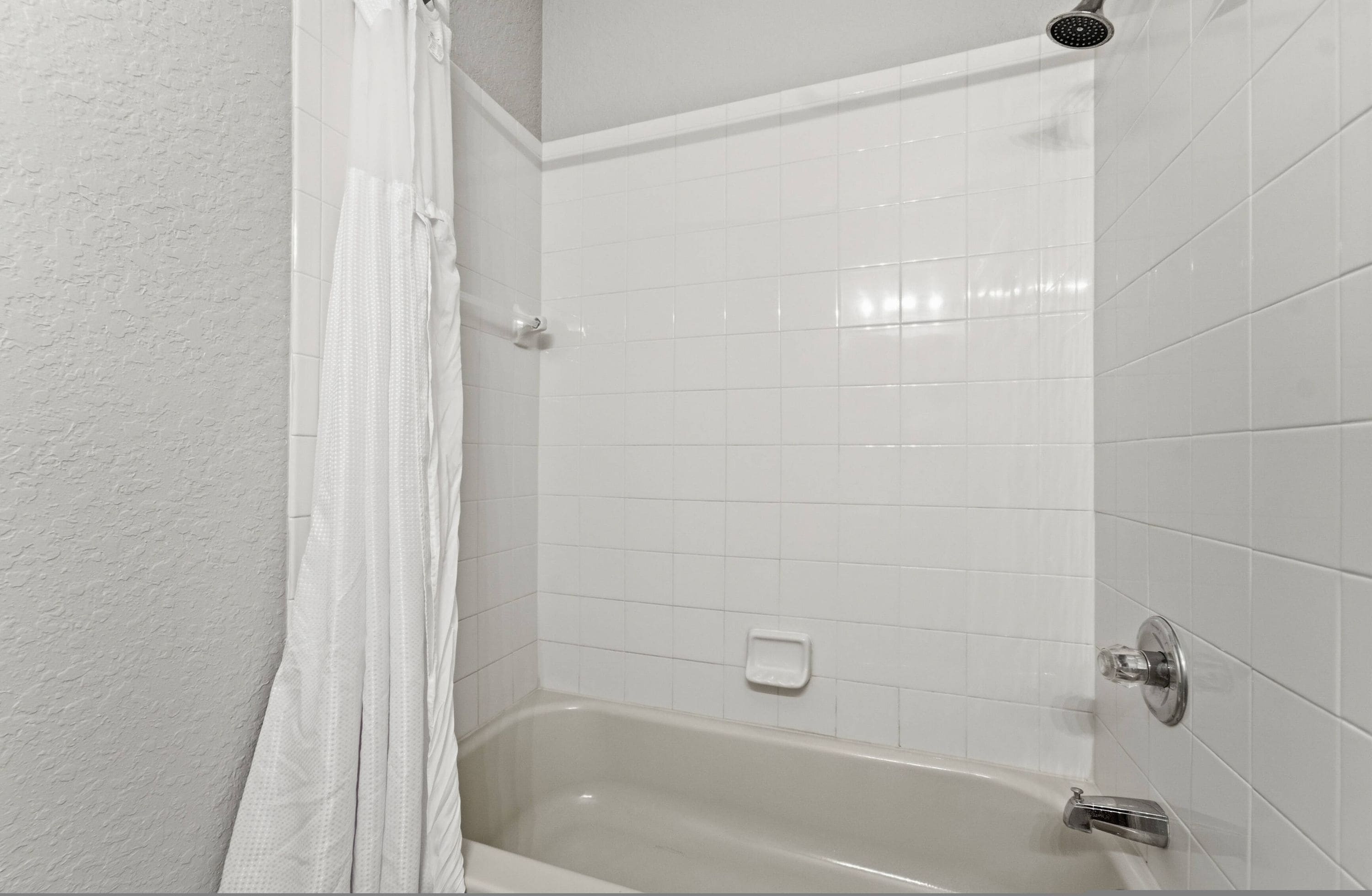 A bathroom with a bathtub, white tiled walls, and a shower curtain.