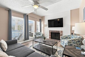 A living room with a fireplace, sofa, armchair, and a flat-screen TV. - Modern 2BR Condo in a Prime Walkable Location (Madeira Beach)