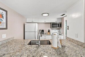 A compact kitchen with white cabinets, a stainless steel sink, a microwave, and a stove. - Modern 2BR Condo in a Prime Walkable Location (Madeira Beach)