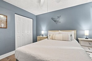 A bedroom with a bed, two bedside tables, a nightstand, a door, and a wall-mounted light fixture. - Modern 2BR Condo in a Prime Walkable Location (Madeira Beach)