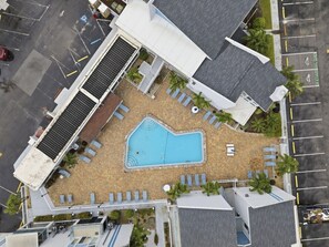 En vy från ovan av ett hotell med en swimmingpool omgiven av solstolar och palmer.