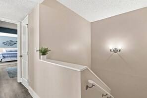 A staircase with a white handrail, a wall-mounted light fixture, and a potted plant. - Modern 2BR Condo in a Prime Walkable Location (Madeira Beach)
