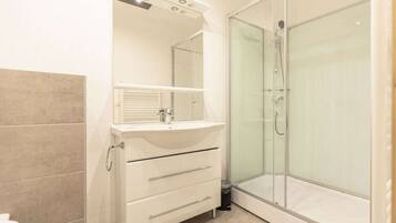 A bathroom with a glass-enclosed shower, a white vanity with a mirror, and a tiled floor.
