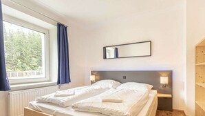 Une chambre avec un lit en bois, une fenêtre avec des rideaux, une table de chevet avec une lampe et un miroir au mur.