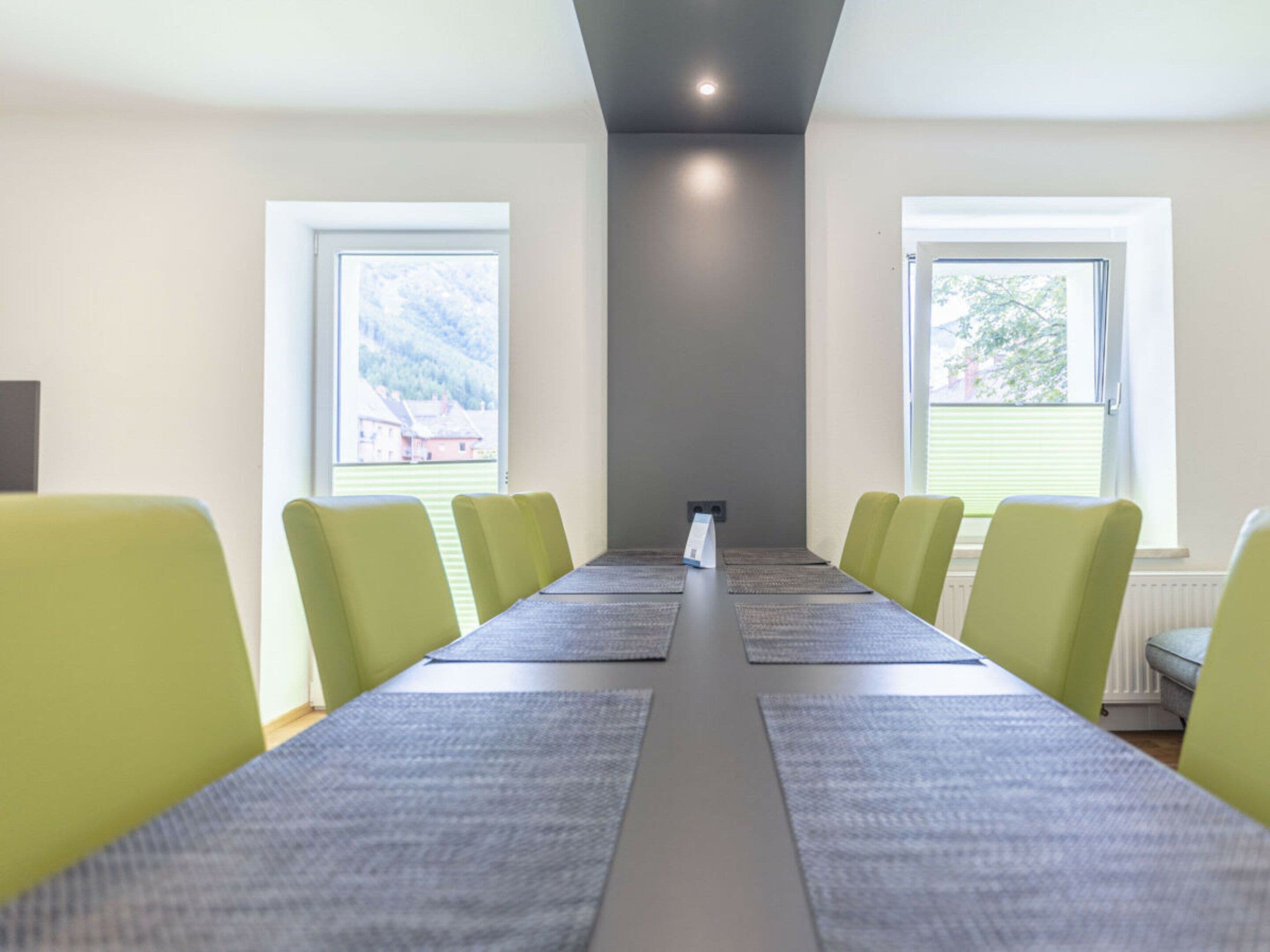 A conference room with a long table and chairs, large windows, and a ceiling light.