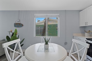 Eine moderne Küche mit weißen Schränken, einem Esstisch mit Stühlen, einer Zimmerpflanze und Blick auf eine grüne Landschaft durch ein Fenster.