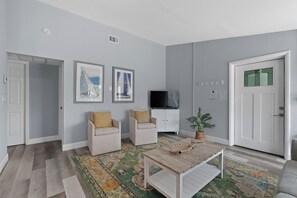 Un salon comprenant un canapé, des fauteuils, une table basse, un téléviseur et une porte avec une fenêtre.