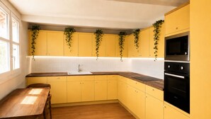 A kitchen with yellow cabinets, a wooden table, and a black oven. - 360° Rooftop, Paris Monuments & Eiffel View from Bed - Artist’s Apt (Paris)