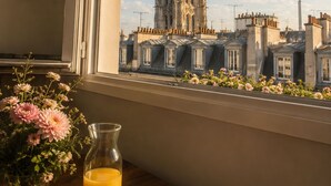 A window view of a historic tower, a table with a plate of fruit, a vase of flowers, and a glass of orange juice. - 360° Rooftop, Paris Monuments & Eiffel View from Bed - Artist’s Apt (Paris)