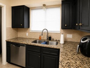 A kitchen with dark cabinetry, a granite countertop, a stainless steel sink, a dishwasher, and a coffee maker.