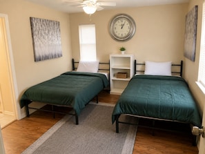 A bedroom with two single beds, a wall clock, a window with blinds, a ceiling fan, and a small shelf with a plant. - Terrific 2-bedroom house minutes from Airport (Humble)