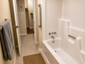 A bathroom with a white bathtub, a towel rack with a towel, a small plant on a shelf, and a door leading to another room. - Terrific 2-bedroom house minutes from Airport (Humble)