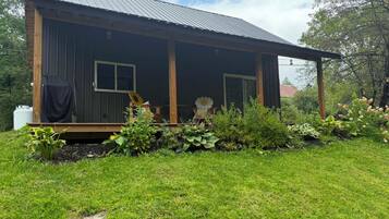 A single-story wooden cabin with a metal roof, surrounded by a well-maintained garden with various plants and flowers.