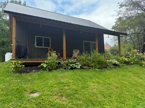 A single-story wooden cabin with a metal roof, surrounded by a well-maintained garden with various plants and flowers. - Tranquil 1-bedroom Brookeview Vermont Cabin in charming Barton (Barton)