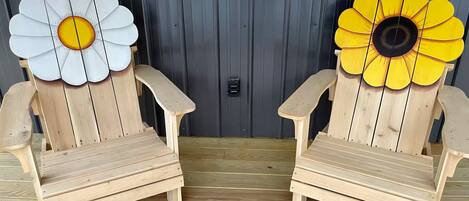 Zwei Holz-Adirondack-Stühle mit großen Blumenornamenten an den Rückenlehnen, vor einer dunklen Holzverkleidung platziert.