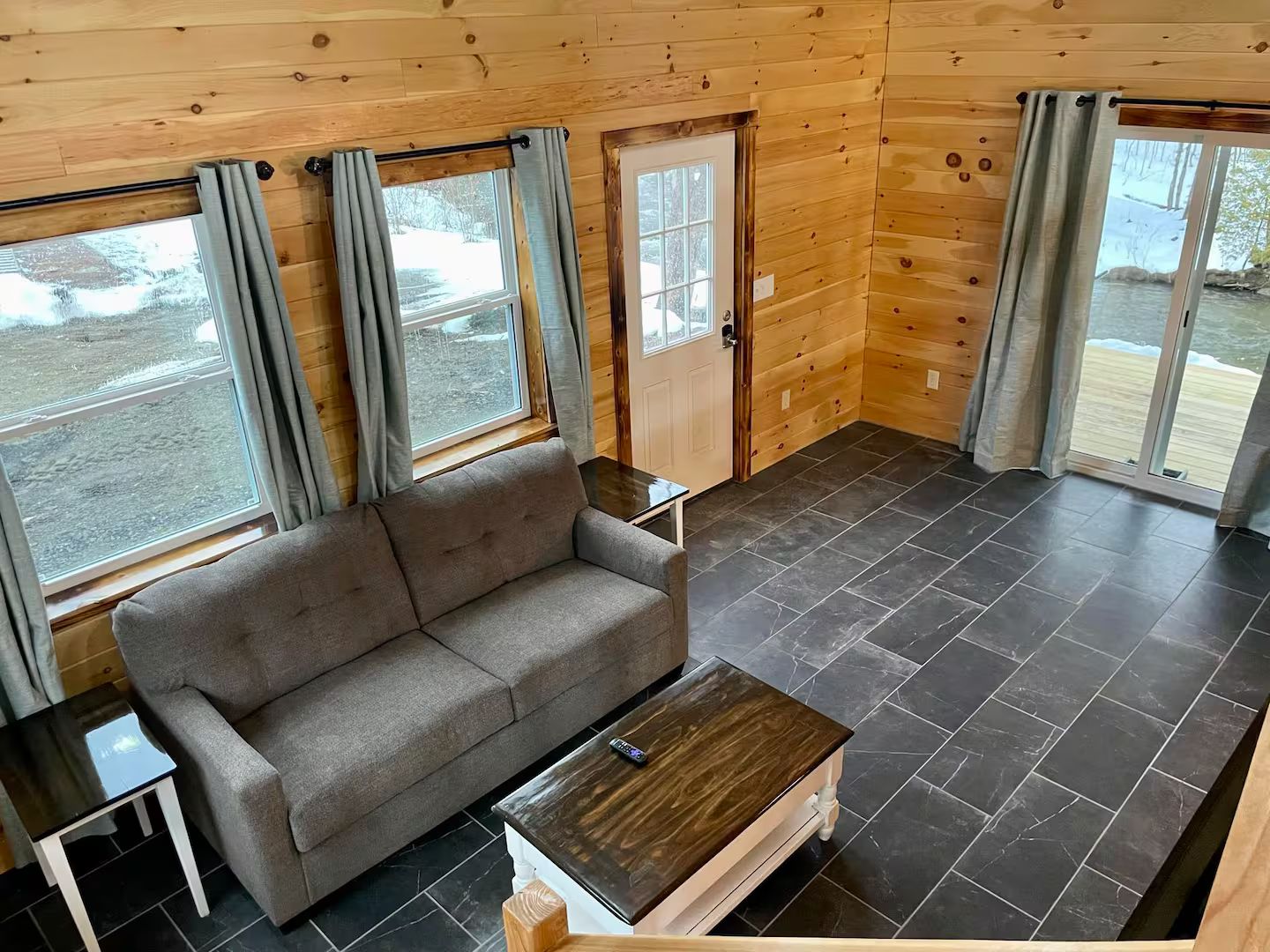 En stuga byggd av timmer med en soffa, ett litet bord och en dörr som leder ut.