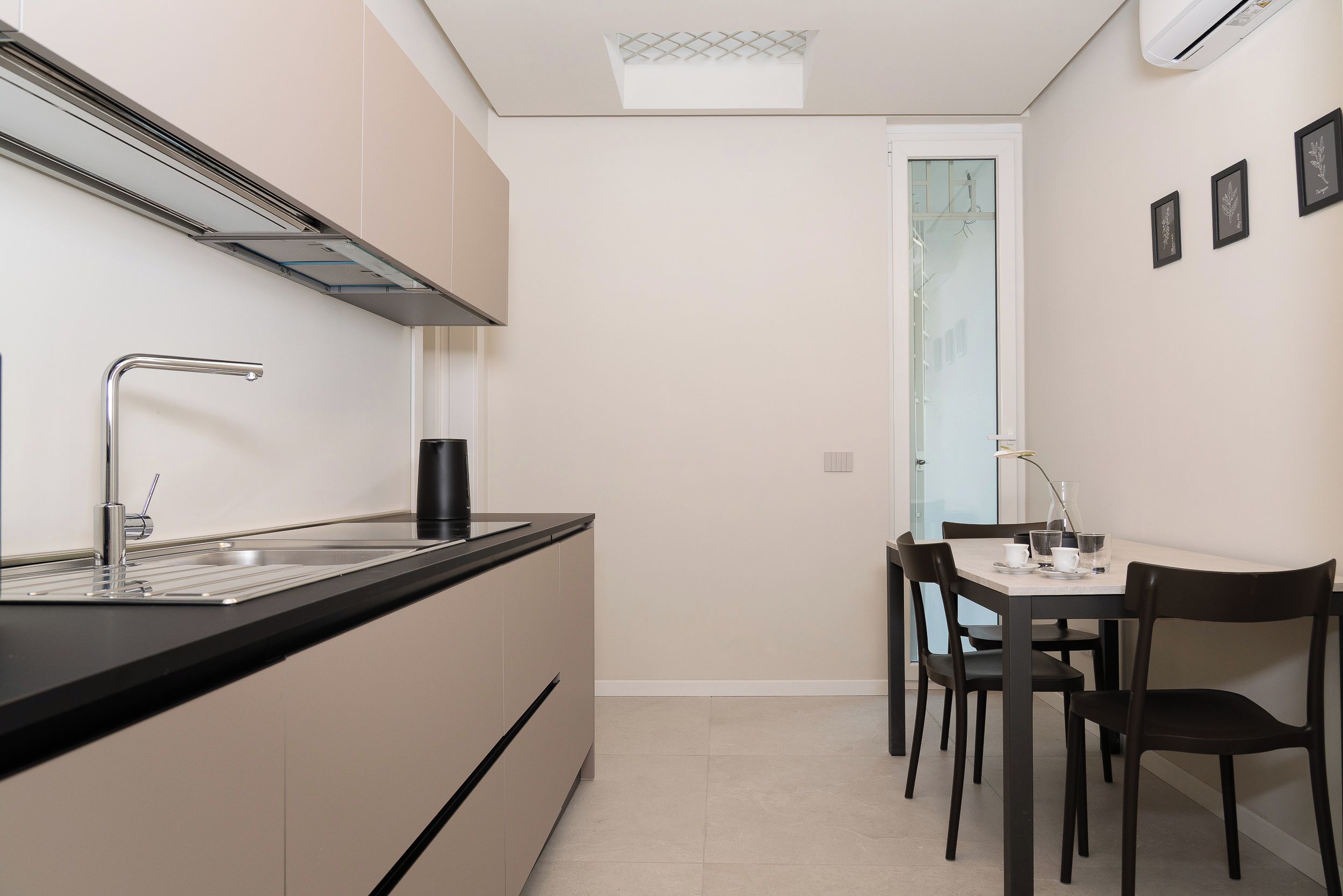 Cozinha compacta com design moderno, destacando uma pia de aço inoxidável, bancada preta e fogão embutido.