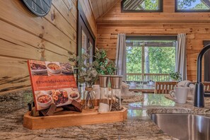 A wooden interior with a kitchen area, a tray with a book titled 'crumbles & cobblers,' and various kitchen utensils. - Bear Bungalow | Mtn & Forest Views | Hot Tub (Sevierville)
