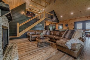 A spacious living room with a large L-shaped sectional sofa, a wooden coffee table, and a staircase leading to an upper level. - Bear Bungalow | Mtn & Forest Views | Hot Tub (Sevierville)