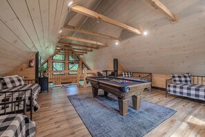 Una habitación acogedora con mesa de billar, un sofá y una cama con ropa de cama a cuadros.