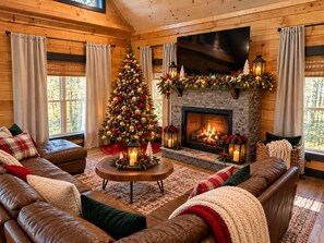Un interior acogedor de cabaña de troncos con chimenea, un árbol de Navidad, sofás de cuero y un ventanal grande.