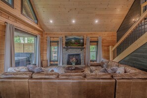 A cozy living room with a fireplace, leather sofas, and a television. - Bear Bungalow | Mtn & Forest Views | Hot Tub (Sevierville)