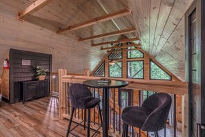 A wooden interior with a high ceiling, a staircase, and a seating area with two chairs. - Bear Bungalow | Mtn & Forest Views | Hot Tub (Sevierville)