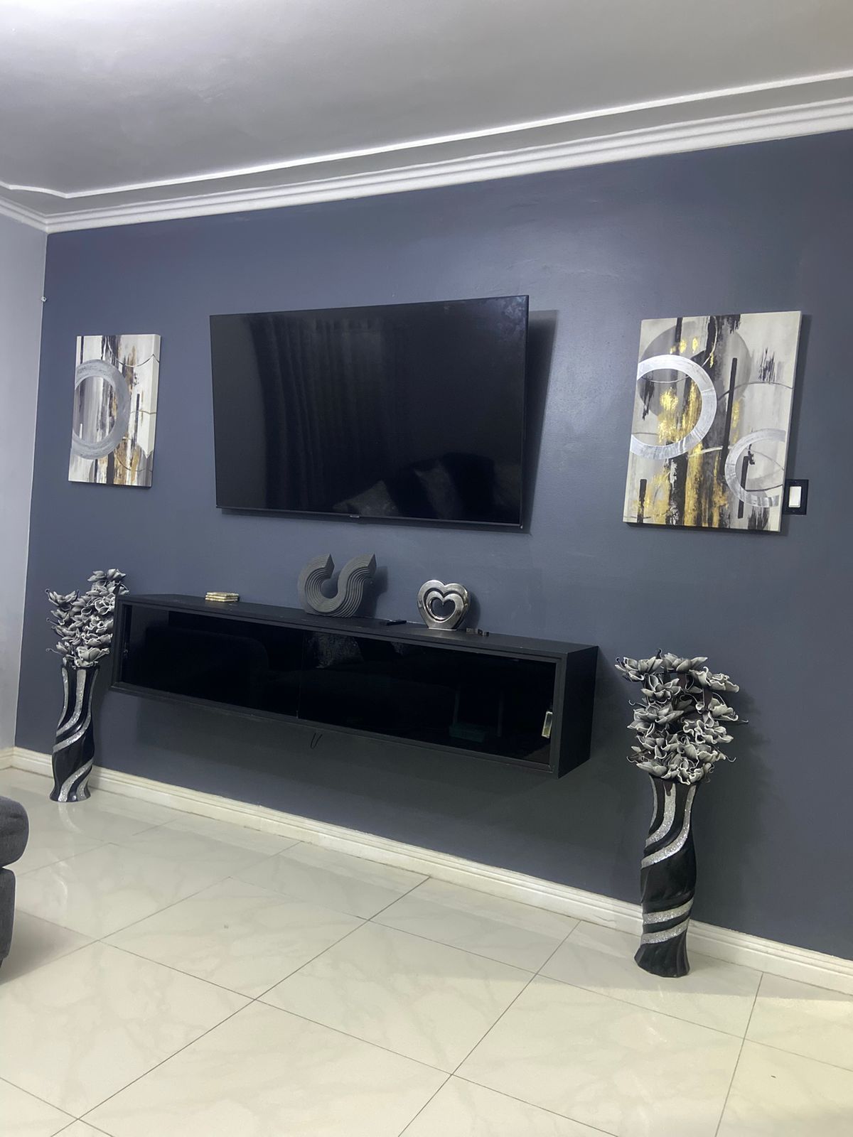 A living room with a flat-screen TV mounted on the wall, a black entertainment unit below, and two decorative vases on either side.
