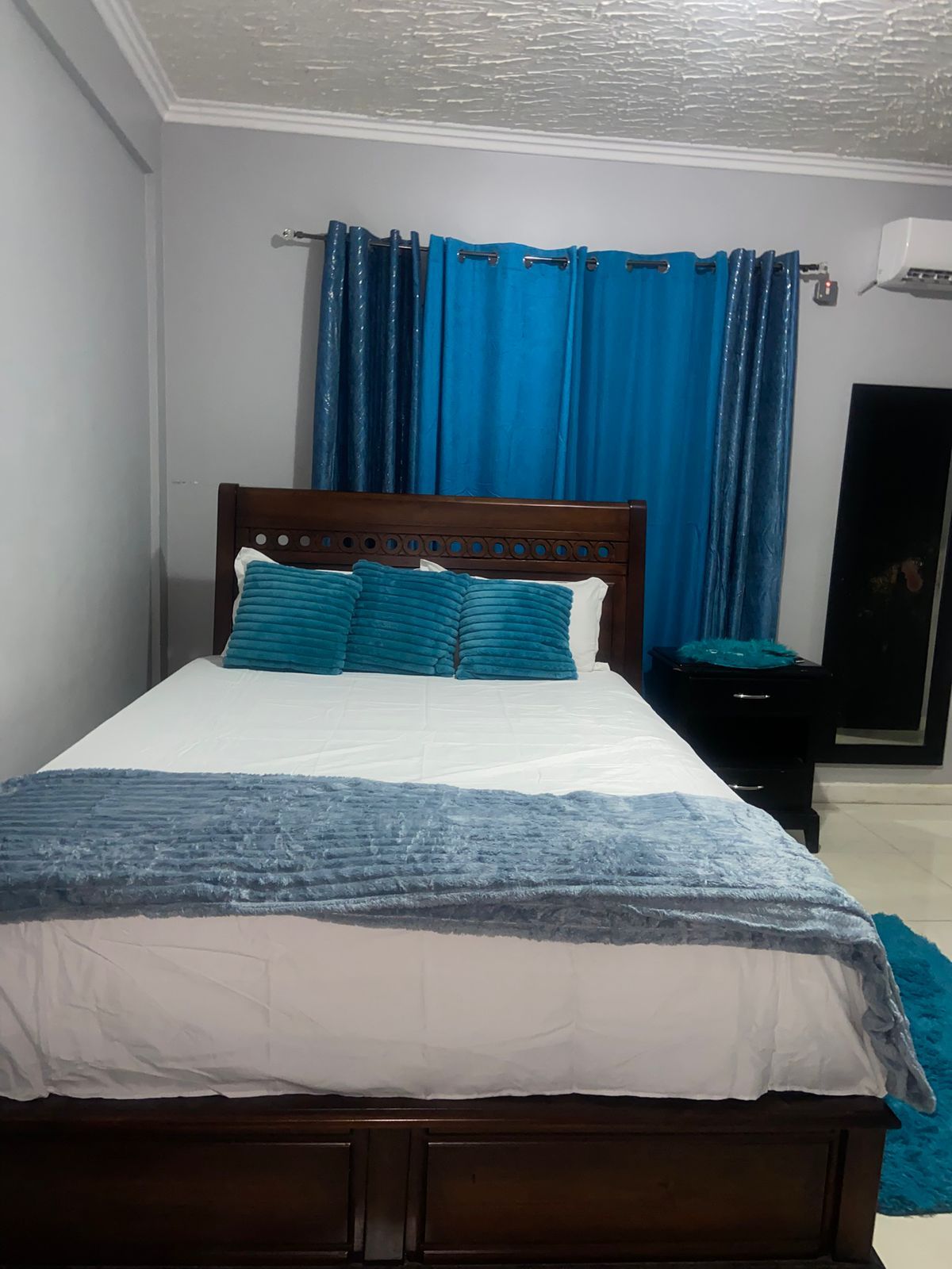A bedroom with a wooden bed, blue curtains, and a white wall.