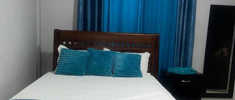 A bedroom with a wooden bed, blue curtains, and a white wall.