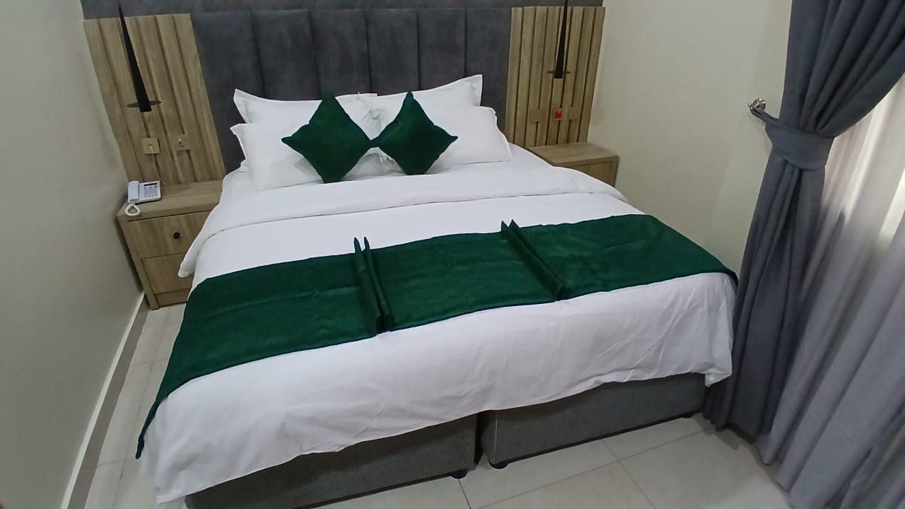 A neatly made bed with a green and white bedspread, a wooden headboard, and a bedside table with a phone.