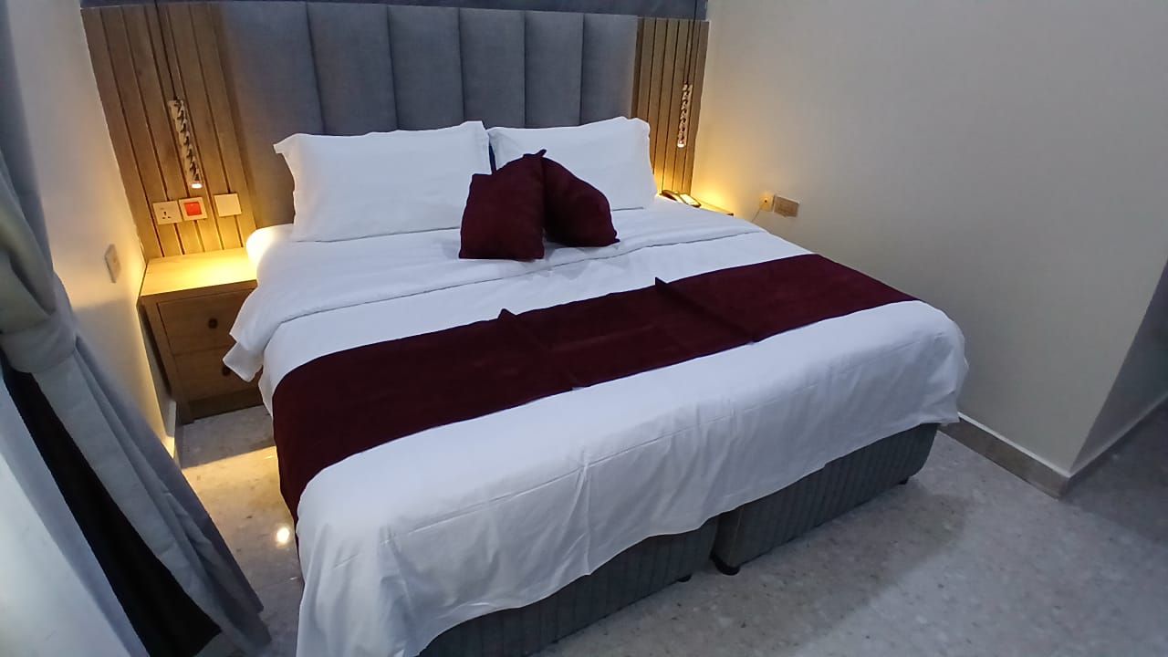 Ein ordentlich bezogenes Bett mit weißer und roter Bettwäsche, einem grauen Kopfteil und Nachttischlampen.