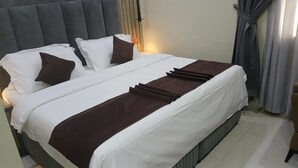 Una cama bien hecha con ropa blanca y marrón, un cabecero y una mesita de noche con una lámpara.