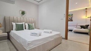 Un dormitorio moderno con una cama grande, una mesita de noche, un adorno en forma de corazón en la pared y vista a otra habitación.