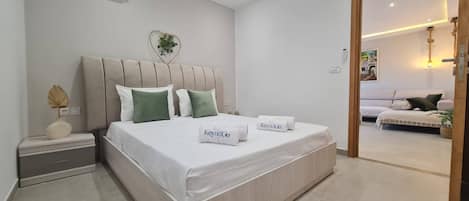 A modern bedroom with a bed, bedside tables, and a view into another room.