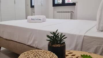 Une chambre à coucher moderne avec un lit, une table de chevet agrémentée d’une plante et un pouf en fibres tressées.