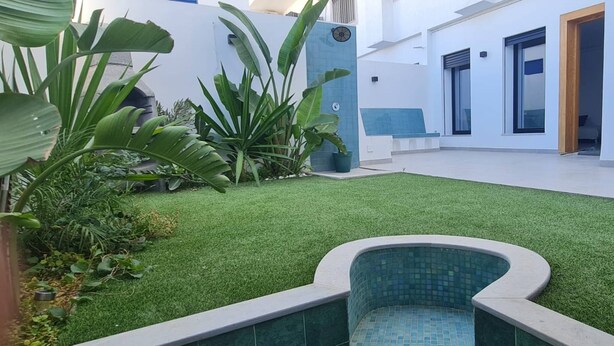 Un espacio exterior moderno con césped artificial, una piscina pequeña y plantas en macetas.