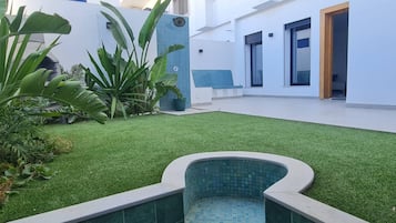 Área externa moderna com grama sintética, uma piscina pequena e plantas em vasos.