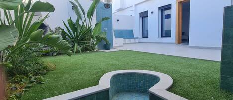 Un espacio exterior moderno con césped artificial, una piscina pequeña y plantas en macetas.